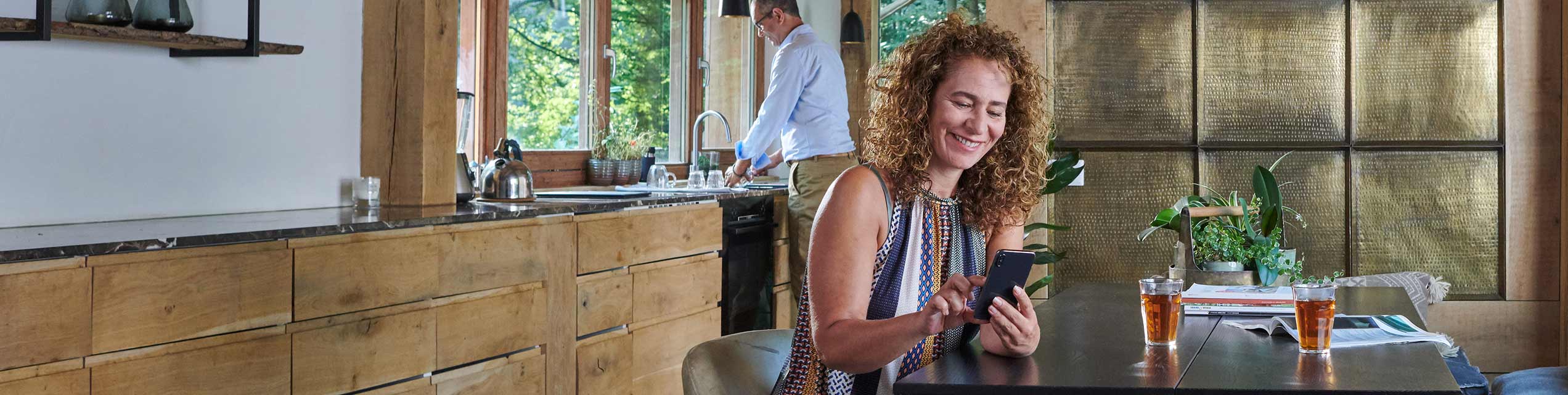 Vrouw zit aan de keukentafel en kijkt naar haar mobiele telefoon